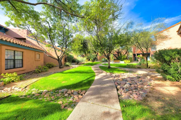 Concrete pathway in the middle of mediterranean homes at Tucson, Arizona. Walkway heading to the entrance of the houses on both sides with stones on the lawn at the front.