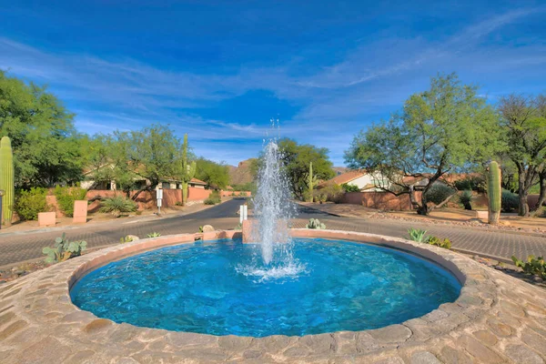 Rotational road with water fountain in the middle at the suburbs of Tucson, Arizona. There is a water fountain in the middle against the view of tall cactus and trees near the houses.