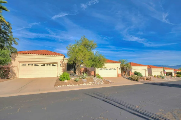 Attached garages in a subdivision at Tucson, Arizona. There is an asphalt road with cracks at the front of the driveway with white garage doors and concrete tile roofs against the blue sky.