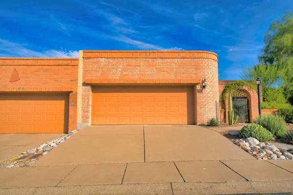 Two garage doors with wall bricks at Tucson, Arizona. Garage exterior with concrete driveways near the single gate with cactus and lamp post at the front.