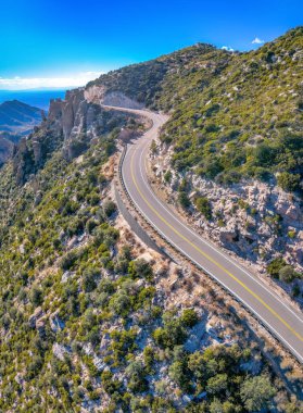 Winding road in a high angle view at the middle of the rocky mountain range slopes at Tucson, AZ. Highway on a mountain range with trees against the blue sky background.