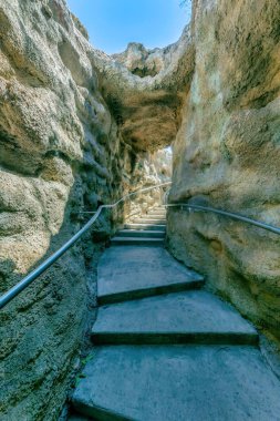 Narrow pathway with concrete steps in between the rock walls in San Antonio, Texas. Stairs with metal handrails inside a rock walls with direct sunlight.