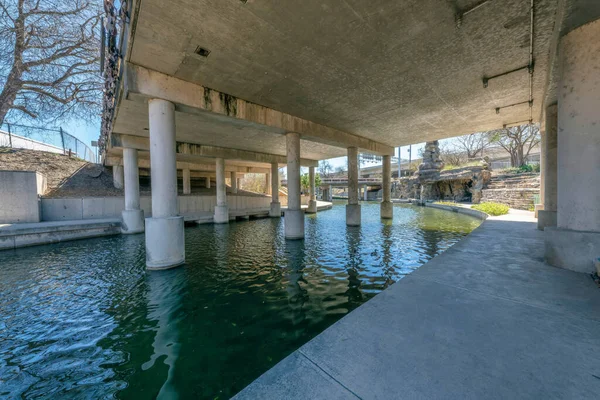 Concrete walkway near the river under a bridge at San Antonio, Texas. View of a concrete bridge and pillars from below at the walkway with curved path near the other bridge at the back.