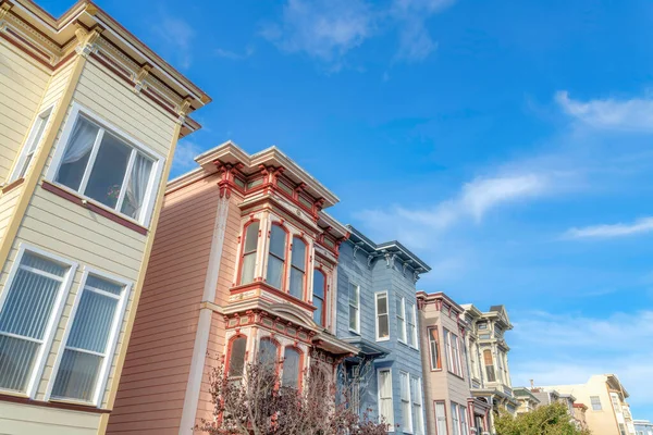 Low angle view of townhouses with colorful wood sidings in San Francisco, California. Residential building exterior with trees at the front and sky at the background.
