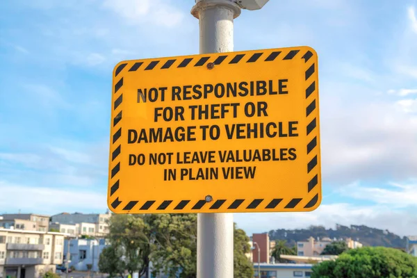 Yellow warning sign on a post in San Francisco, California. Signage with a message, not responsible for theft or damage to vehicle against the view of buildings at the back.