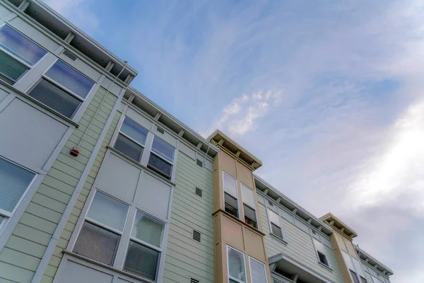 Low angle view of an apartment with wall vents and single hung windows in San Francisco, California. Building with sage green vinyl lap sidings and a sky background.