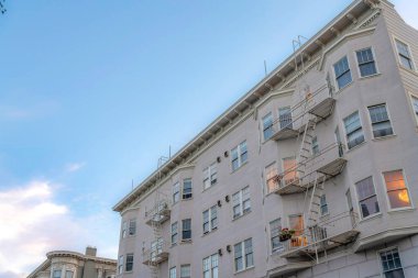 Apartment building with beige exterior and emergency stairs exit in a low angle view. Residential building in San Francisco, California with bay windows against the sky at the background.