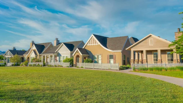 Panorama Whispy white clouds Fenced residential houses with path and lawn at the front in Daybreak, South Jordan, Utah. Exterior of houses with traditional and french country designs