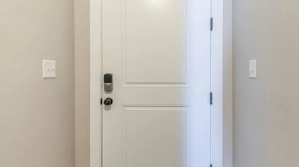Panorama White fire door with a digital access to the garage. Interior of the house with light gray wall and dark wood flooring at the garage entrance.
