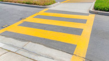 Panorama Yellow pedestrian lanes at the crosswalk in Ladera Ranch, California. Two road lanes with island in the middle with shrubs and a view of the concrete sidewalk across the street.
