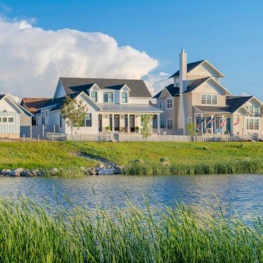Square White puffy clouds Panoramic view of blue waters of Oquirrh Lake at Daybreak in South Jordan, California. Residential area with lake waterfront with tall grasses at the front.