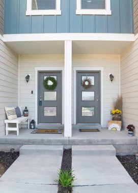 Vertical Two gray front door of a townhouse with two concrete entrance way. Home entrance with decorated doors with wreath and glass panels in the middle of a wall with vinyl wood and stone