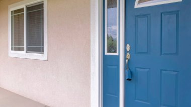 Panorama Blue front door with lockbox, arched glass panes and sidelights. Entrance of a house with beige siding and window with white frames with shrubs at the front.