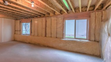 Panorama Unfinished basement with plastic vapor barrier and windows. Interior of a basement with wooden ceiling beams with metal pipe and light bulbs.