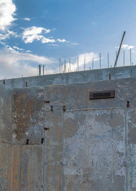 Vertical White puffy clouds Underground support of a house with concrete walls. Home basement foundation exterior in a low-angle view against the sky with clouds.