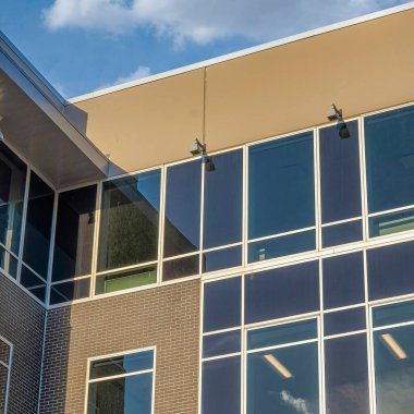 Square White puffy clouds Building with ip dome security camera at the corner top. Low angle view of a building with an exterior of a glass and brown bricks wall claddings.