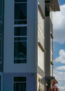 Vertical White puffy clouds Sunset reflecting on to the glass walls of the building. Exterior of a building with security camera on the side and an exterior of concrete, bricks and glass walls.
