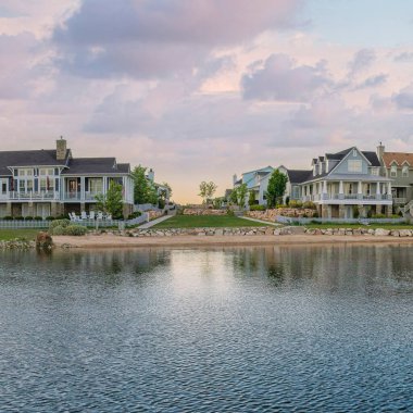 Square Puffy clouds at sunset Panoramic view of Oquirrh Lake with reflective water at Daybreak, Utah. There are large residential buildings and mountains on the right at the back.
