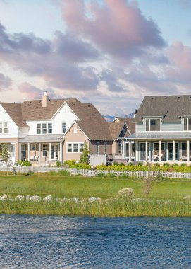 Vertical Puffy clouds at sunset Oquirrh Lake at the front of large residential buildings at Daybreak, Utah. There is a large green field near the white picket fence at the front of colorful houses