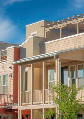 Vertical Whispy white clouds Complex residential houses with coral pink and beige tones at Daybreak, South Jordan, Utah. Exterior of complex buildings with balconies and pergola at the roof tops.