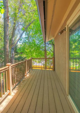 Vertical Wooden deck of a house with a view of trees outside. Terrace of a house with sliding glass door on the left and a wooden flooring and handrails.