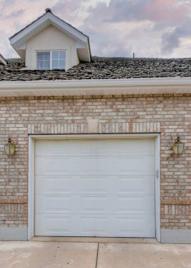 Vertical Puffy clouds at sunset Garage exterior with bricks and three white sectional doors. There are two attic windows and chimney