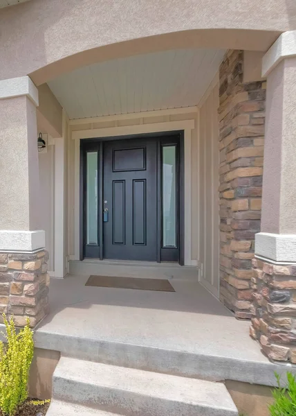 Vertical Whispy white clouds Facade of a front exterior of a house with front yard garden. Porch with black front door with lockbox and two side panels near the windows and a wall