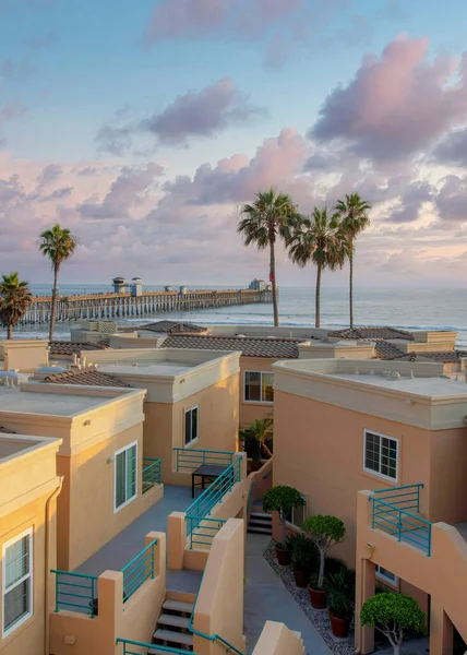 Vertical Puffy clouds at sunset View of roof decks of complex buildings with beach waterfront at Oceanside, California. There are views of palm trees and piers on the beach against the sunset sky.