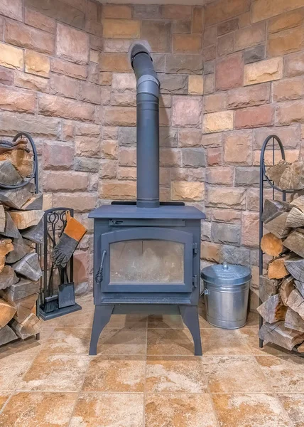 Vertical Interior of a fireplace with vintage wood burning stove. Fire place with craftsman design interior and firewood stocks on a stand against the stone walls.