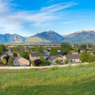 Kare Fısıldayan Beyaz Bulutlar, Utah, Daybreak 'te dağ sıraları olan bir yerleşim bölgesinin panoramik görüntüsü. Çitlerle çevrili yerleşim alanının yakınında büyük bir çim tarlası var..