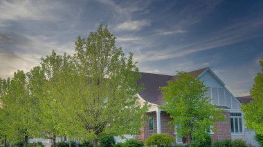 Panorama Fısıldayan Beyaz Bulutlar Köşesi evi tuğla kaplamalı, çiçekler ve ağaçlar Utah, Daybreak 'te çimenlikte. Evlerin önündeki kaldırımlar ve yollar ile birlikte sütun ağaçlarının olduğu yerleşim alanı..