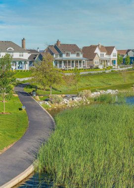 Utah 'ta Şafak vakti, üzerinde asfalt kaldırım olan dikey Whispy beyaz bulutları Oquirrh Gölü. Gölün üzerinde bir köprü ve arka planda dağlara karşı farklı yapılara sahip evler var..