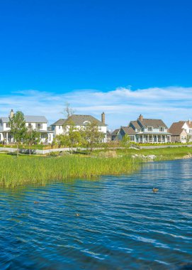 Utah, Daybreak 'te bir yerleşim alanının ortasında dikey Whispy beyaz bulutları. Gölün kıyısında asfalt bir yol var ve arka planda renkli evler var..