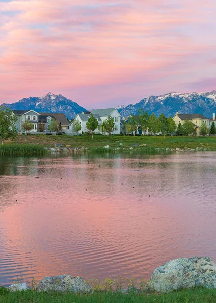 Vertical Reflective Oquirrh Lake waterfront Daybreak, Utah. Panoramic view of the lake at the front of the houses and fields against the mountain range and sky with pink hue.