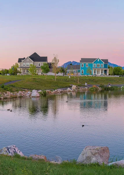 Vertical Reflective Oquirrh Lake waterfront at Daybreak, Utah. Panoramic view of the lake at the front of the houses and fields against the mountain range and sky with pink hue.