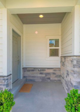 Yan tarafında gri kapılı bir evin dikey girişi ve sütun direğinin yanında iki saksı bitkisi. Bodrum pencereleri, beyaz vinil ahşap ve taş kaplamaları olan ev dışı..