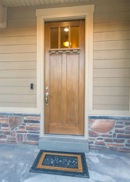 Cam camları ve şık paspası olan dikey ahşap ön kapı. Korkulukları ve bej vinil ahşap ve taş kaplamaları olan bir evin ön sundurması..