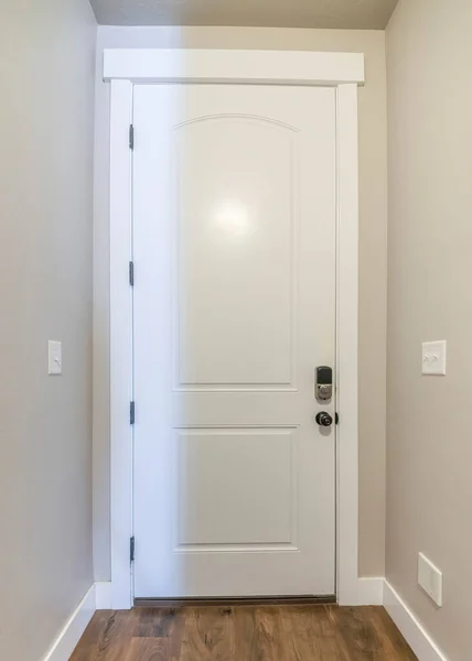 Vertical White fire door with a digital access to the garage. Interior of the house with light gray wall and dark wood flooring at the garage entrance.
