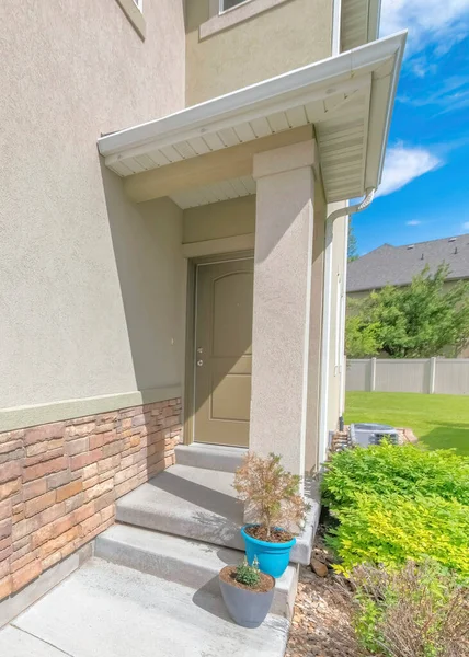 Vertical Whispy white clouds Entrance of a house at the side of the wall with stone veneer. Front door with potted plants on the concrete steps beside the bushes and green lawn against the vinyl fence and neighbor\'s house.