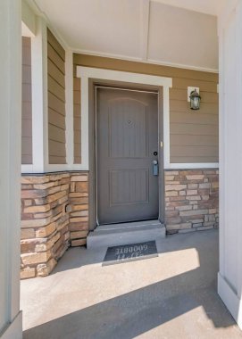 Beyaz sütun direkleri ve kırmızı kol sandalyesi olan bir evin dikey verandası. Taş kaplamalı bir evin dış cephesi ve kilitli kahverengi bir ön kapısı var..