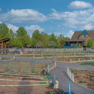 Utah, Daybreak 'teki bir yerleşim bölgesinde beyaz çitli beyaz bulutlu halk bahçesi. Çakıl yolu ve arka planda evler ve tarlalar olan organize bir bahçe yatağında ekinler var..