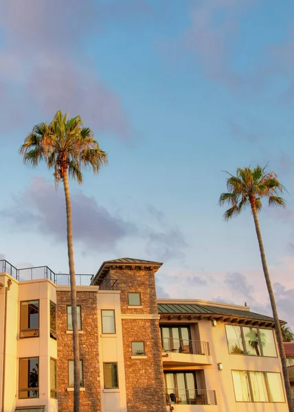 Vertical Puffy clouds at sunset Oceanside building rentals in a low angle view at California. Large building exterior with balconies and railings on the rooftop and palm trees at the front.