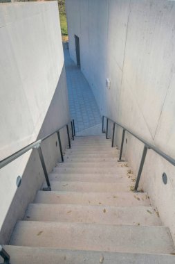 Staircase with metal handrails leading down to a stone tile pavement at Austin, Texas. Staircase with concrete steps in the middle of concrete walls.