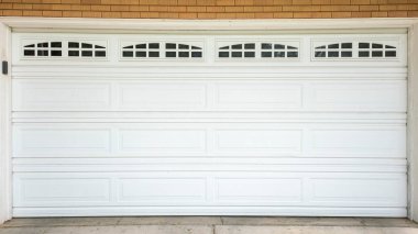 Panorama White sectional garage door with window panels and concrete driveway. Exterior of a garage of a house with brown bricks wall siding.