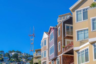 Row of four-storey houses with a view of neighborhood on a mountain slope near the Sutro Tower. View of houses with corner balconies and casement windows near the tower in San Francisco, CA.
