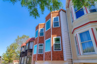 Bay windows of an adjacent houses with wood shingle sidings at San Francisco, California. Side view of houses with reflective glass panes against the trees and clear sky background.