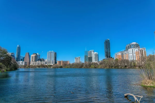 View of low-rise to high-rise buildings across the Colorado River at Austin, Texas. Cityscape of Austin reflecting on the water at the front against the clear sky.