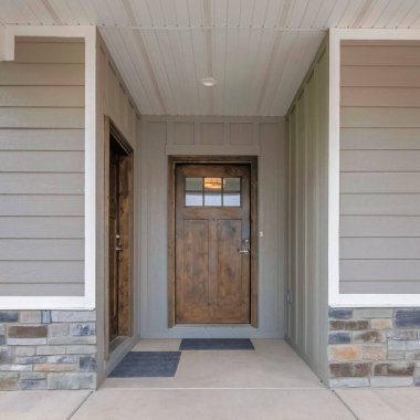 Saksı çiçekli ve iki ahşap ön kapısı olan bir evin kare verandası. Gri vinil ahşap ve taş kaplamalı bir evin dışı..