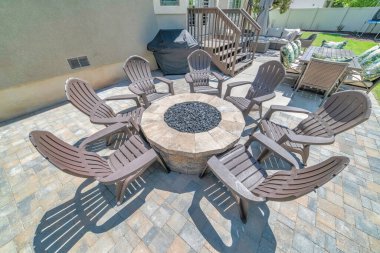 Yuvarlak ateş çukurunun etrafında ahşap sandalyeler olan bir evin arka avlusu. Bu güneşli iskan güvertesinde yemek için masa ve sandalyeler ve dinlenmek için kanepe de görülebilir..