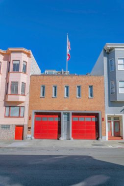 Açık mavi gökyüzünde kırmızı garaj kapısı ve bayrağı olan bir binanın önü. Güneşli bir günde San Francisco 'da evleri olan bir binanın cephesi.